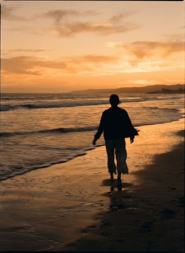 A silhouetted figure walking along a beach at dusk with gentle motion blur.
